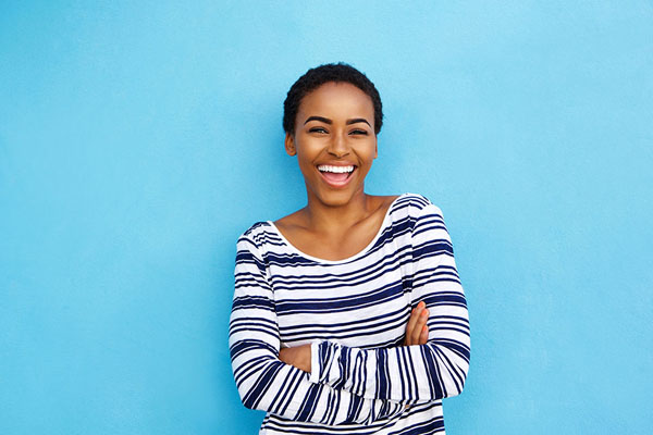 young woman in striped shirt smiling with her new porcelain veneers in front of a blue background